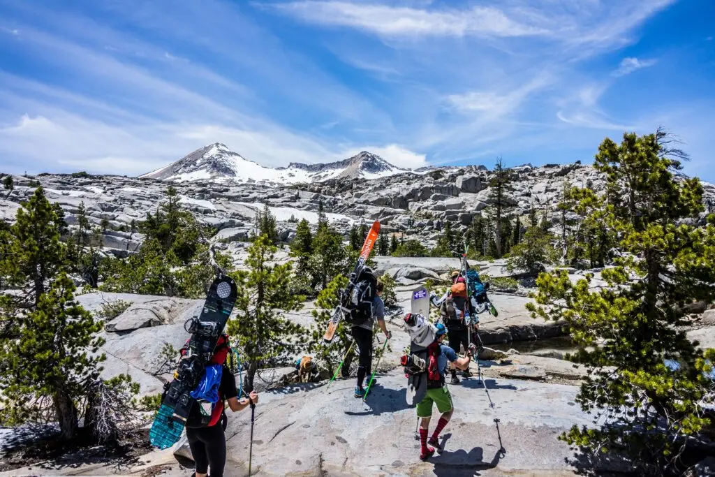 Group of adventurous skiers hiking up a snowy mountain with gear in Rocky terrain.