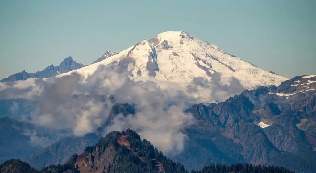 A scenic view of a snow-covered mountain peak surrounded by clouds and a clear blue sky.